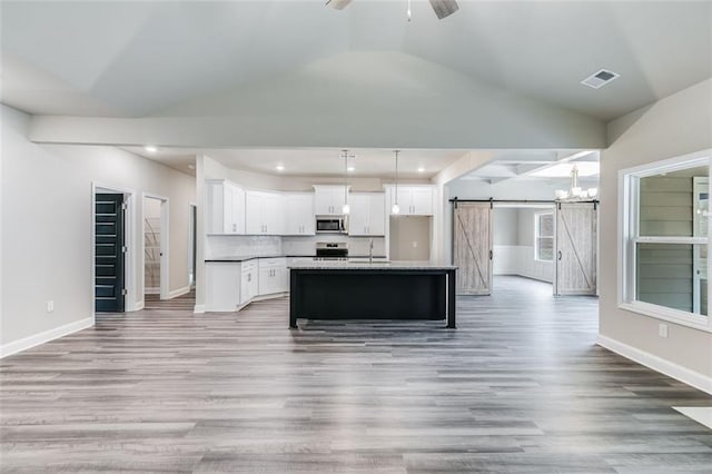 kitchen featuring appliances with stainless steel finishes, light wood-type flooring, a kitchen island with sink, a barn door, and white cabinets