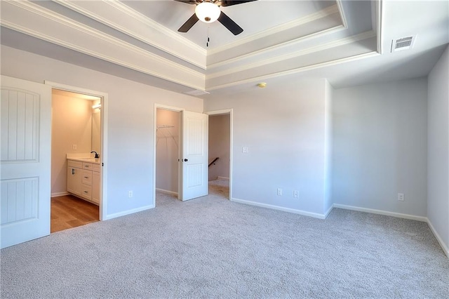 unfurnished bedroom featuring ceiling fan, a closet, light carpet, a tray ceiling, and a walk in closet