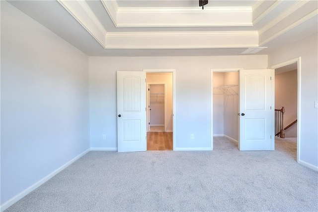 unfurnished bedroom featuring a walk in closet, a raised ceiling, ornamental molding, and carpet flooring