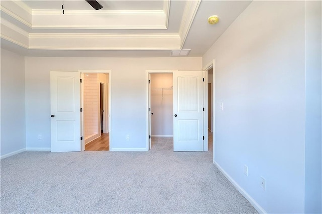 unfurnished bedroom featuring carpet, baseboards, a tray ceiling, ornamental molding, and a spacious closet