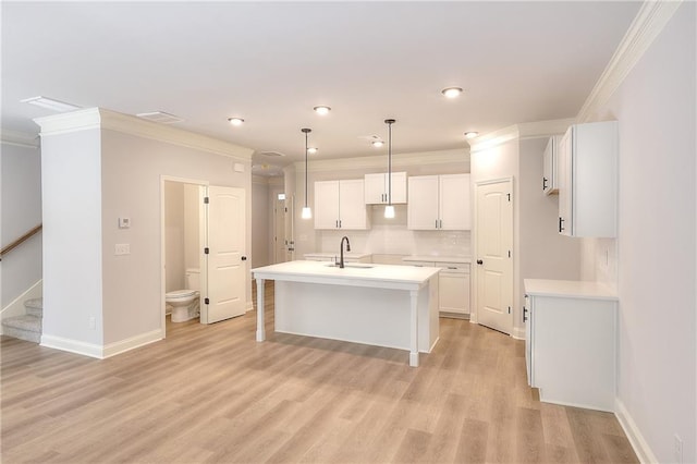 kitchen featuring an island with sink, light hardwood / wood-style floors, hanging light fixtures, white cabinetry, and ornamental molding