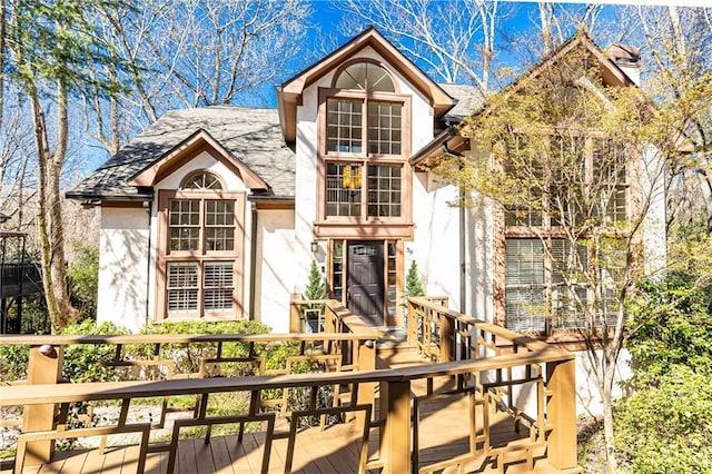 view of front of property with stucco siding, a wooden deck, and a shingled roof