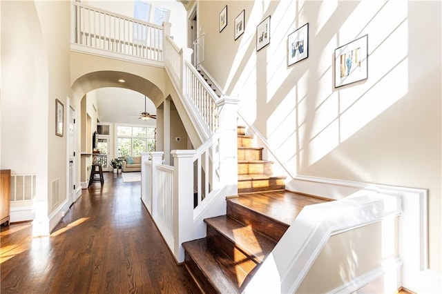 stairway featuring visible vents, ceiling fan, a towering ceiling, wood finished floors, and arched walkways