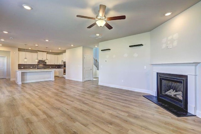unfurnished living room featuring ceiling fan, light wood-type flooring, and sink
