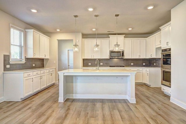 kitchen featuring appliances with stainless steel finishes, a center island with sink, white cabinetry, and pendant lighting