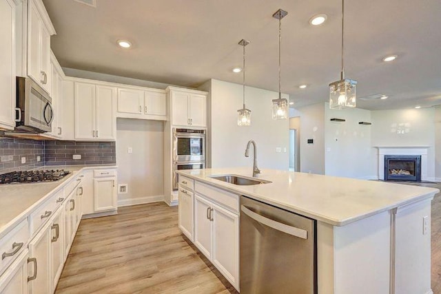 kitchen with a kitchen island with sink, sink, pendant lighting, and appliances with stainless steel finishes