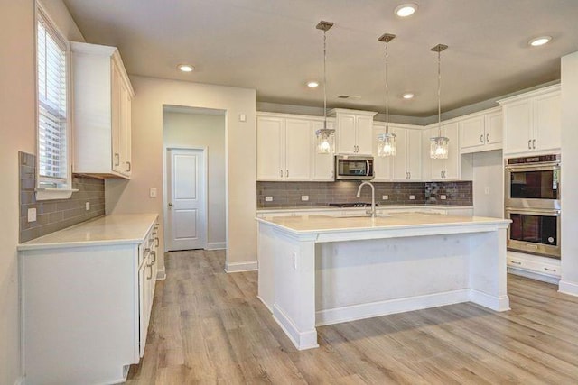 kitchen featuring decorative light fixtures, white cabinetry, stainless steel appliances, and a kitchen island with sink