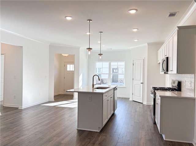 kitchen with dark hardwood / wood-style flooring, stainless steel appliances, sink, pendant lighting, and a center island with sink