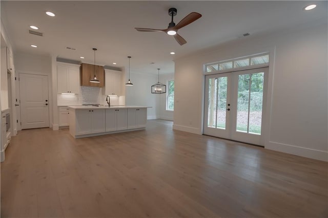 kitchen featuring hanging light fixtures, backsplash, an island with sink, white cabinets, and french doors