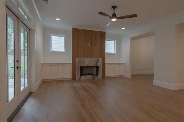 unfurnished living room with crown molding, light hardwood / wood-style floors, a premium fireplace, and french doors