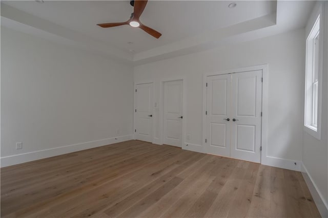 unfurnished bedroom with multiple closets, ceiling fan, a raised ceiling, and light hardwood / wood-style floors