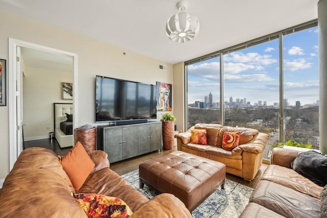 living area with floor to ceiling windows, wood finished floors, visible vents, and baseboards