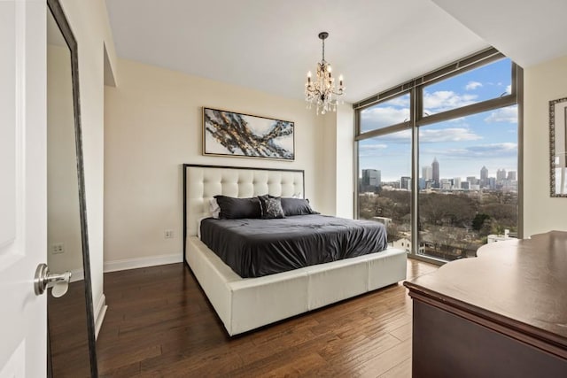 bedroom featuring wood finished floors, baseboards, access to exterior, expansive windows, and a city view