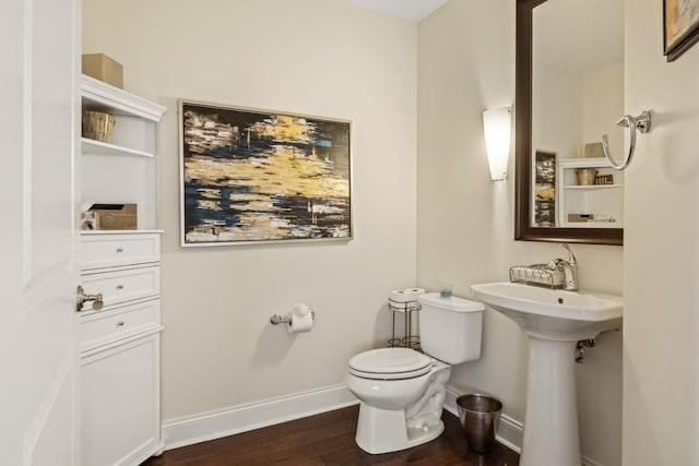 half bath with toilet, wood finished floors, baseboards, and a sink