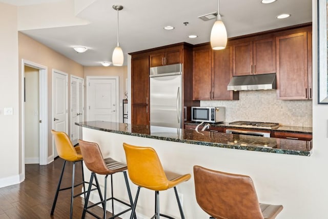 kitchen with visible vents, under cabinet range hood, dark wood finished floors, decorative backsplash, and appliances with stainless steel finishes