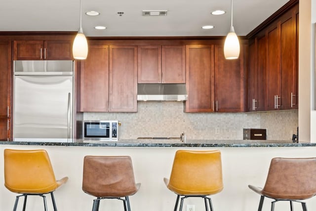 kitchen with visible vents, dark stone counters, stainless steel appliances, decorative backsplash, and under cabinet range hood