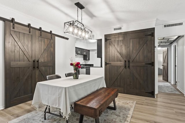 dining room with a barn door, ornamental molding, light hardwood / wood-style flooring, and a textured ceiling