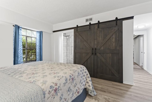 bedroom featuring wood-type flooring, a textured ceiling, crown molding, and a barn door