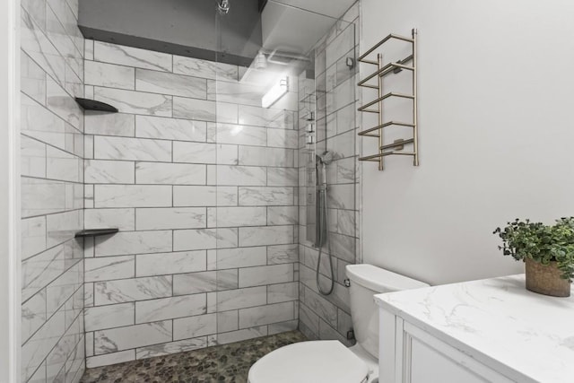 bathroom with a tile shower, vanity, and toilet