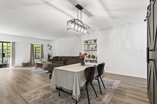 dining area featuring hardwood / wood-style flooring, crown molding, a barn door, and a textured ceiling