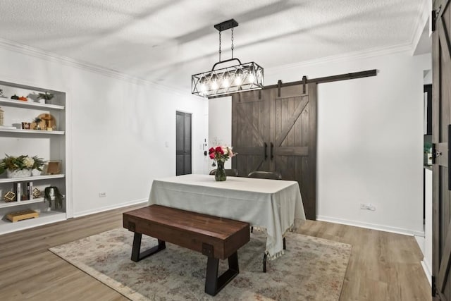 dining area featuring a barn door, ornamental molding, hardwood / wood-style floors, and a textured ceiling