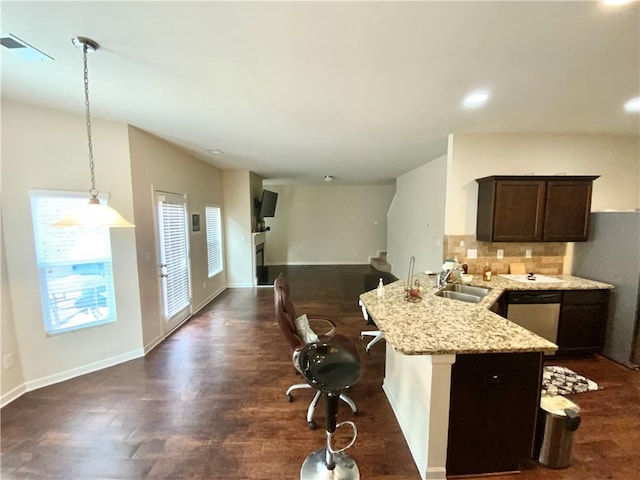 kitchen featuring a peninsula, a sink, stainless steel dishwasher, tasteful backsplash, and decorative light fixtures