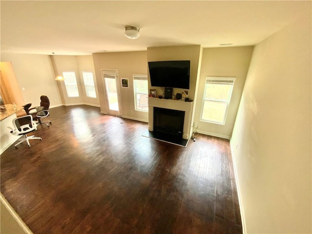 unfurnished living room with dark wood-style floors, a fireplace with raised hearth, baseboards, and a healthy amount of sunlight