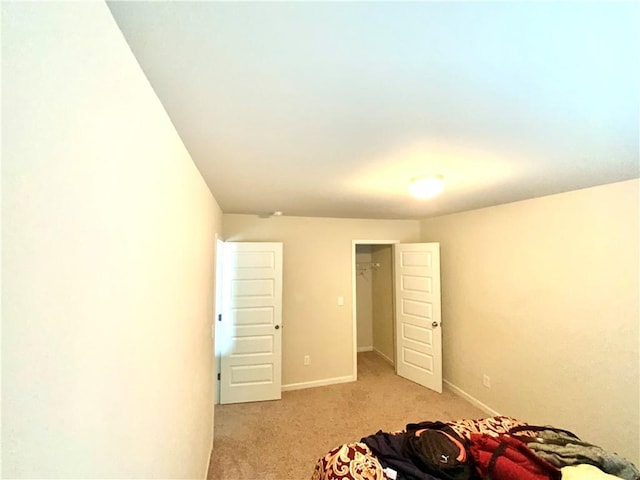 bedroom with baseboards, a walk in closet, and light colored carpet