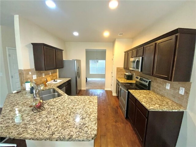 kitchen featuring a peninsula, light stone countertops, stainless steel appliances, and a sink