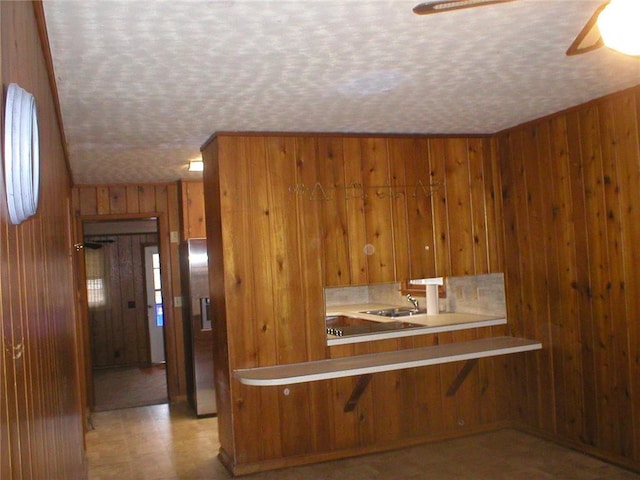 kitchen featuring a breakfast bar, kitchen peninsula, a textured ceiling, and wooden walls