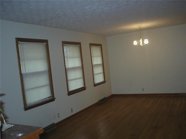 empty room with a chandelier, a textured ceiling, and dark wood-type flooring