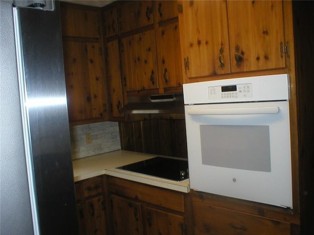 kitchen with black electric stovetop, oven, refrigerator, and decorative backsplash