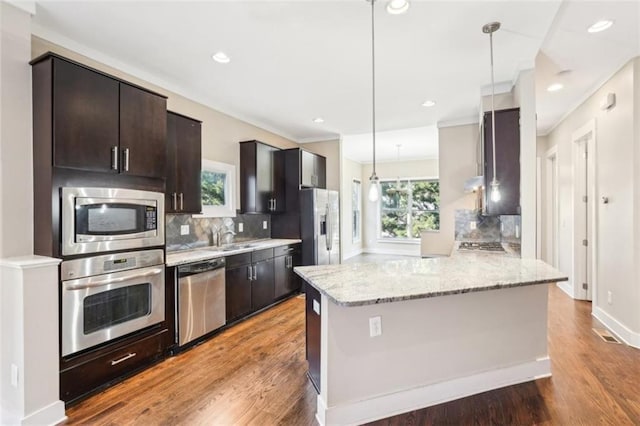 kitchen with wood finished floors, tasteful backsplash, light stone countertops, and stainless steel appliances