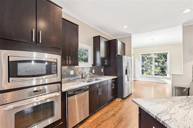 kitchen featuring light wood-style flooring, light stone counters, tasteful backsplash, dark brown cabinetry, and appliances with stainless steel finishes