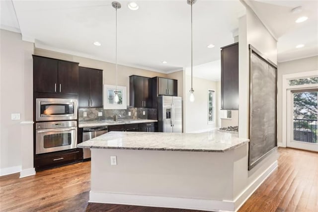 kitchen featuring decorative backsplash, a peninsula, wood finished floors, and appliances with stainless steel finishes