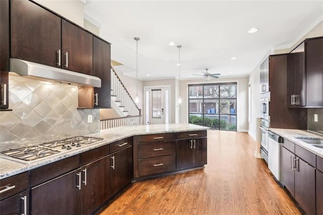 kitchen featuring a ceiling fan, wood finished floors, a peninsula, appliances with stainless steel finishes, and under cabinet range hood