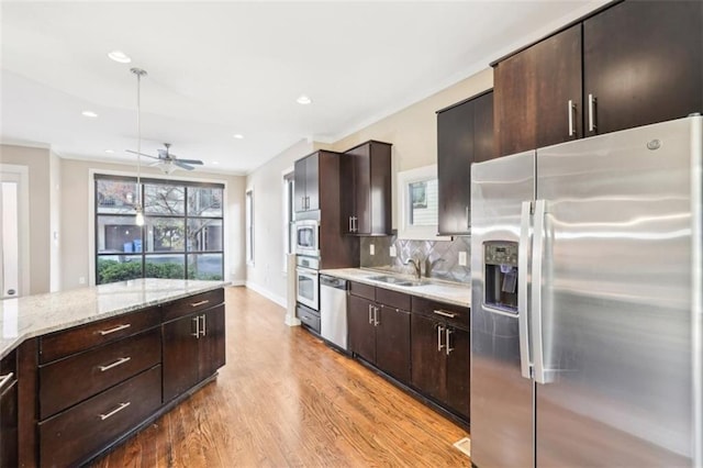 kitchen with a ceiling fan, light wood finished floors, dark brown cabinets, appliances with stainless steel finishes, and backsplash