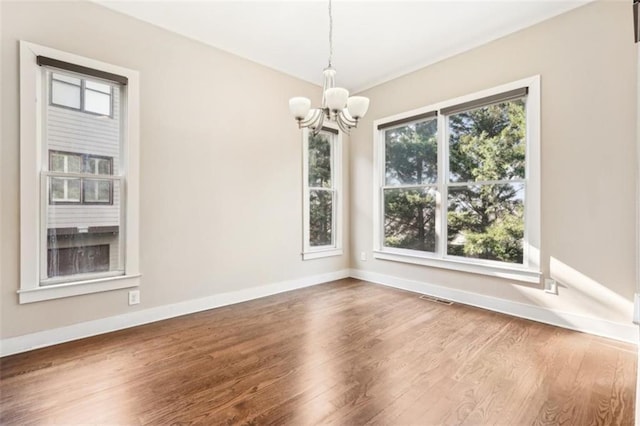 spare room featuring a notable chandelier, baseboards, visible vents, and wood finished floors