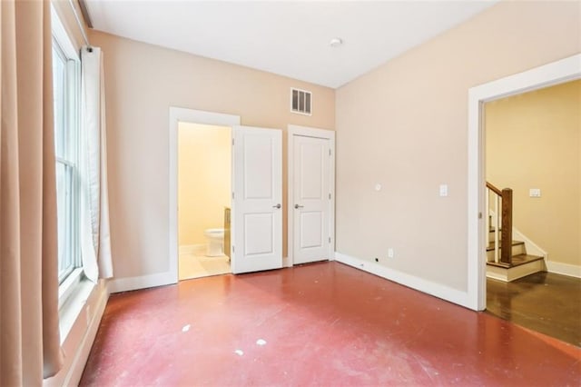 unfurnished bedroom with visible vents, baseboards, concrete floors, and ensuite bathroom