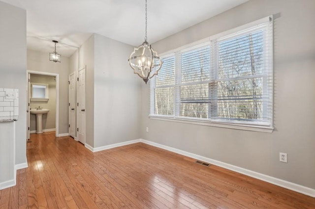 unfurnished dining area featuring a chandelier, a sink, visible vents, baseboards, and light wood-style floors