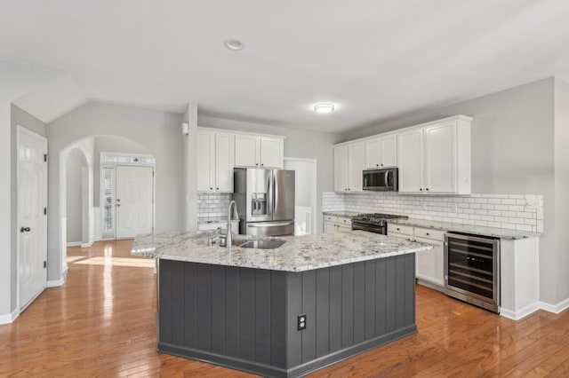 kitchen with appliances with stainless steel finishes, wine cooler, white cabinets, and a center island with sink