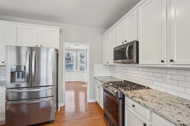 kitchen with light stone counters, stainless steel appliances, backsplash, light wood-style floors, and white cabinets