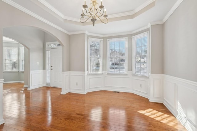 unfurnished dining area with a healthy amount of sunlight, arched walkways, and a raised ceiling