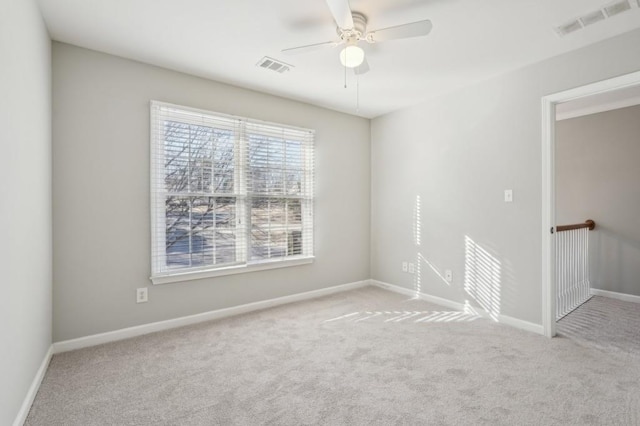 spare room with a ceiling fan, light colored carpet, visible vents, and baseboards