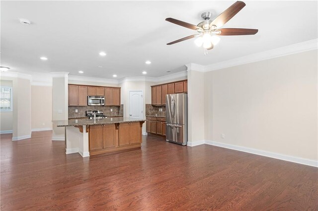 kitchen featuring an island with sink, stainless steel appliances, tasteful backsplash, dark hardwood / wood-style flooring, and crown molding