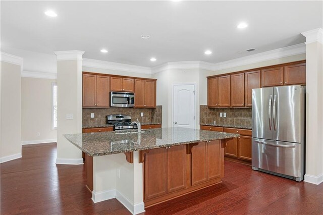 kitchen featuring a center island with sink, stainless steel appliances, decorative backsplash, dark stone countertops, and crown molding