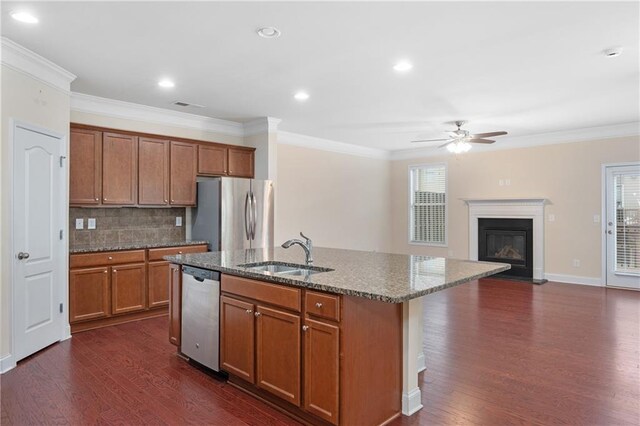 kitchen featuring an island with sink, appliances with stainless steel finishes, backsplash, light stone counters, and sink