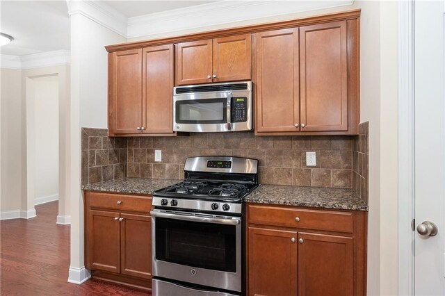 kitchen featuring decorative backsplash, dark stone counters, stainless steel appliances, and ornamental molding