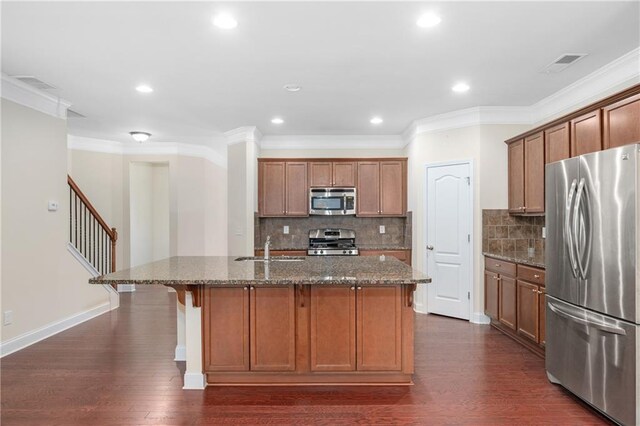 kitchen featuring tasteful backsplash, stainless steel appliances, dark stone counters, and an island with sink