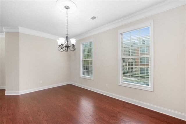 spare room featuring dark hardwood / wood-style flooring, a wealth of natural light, crown molding, and a chandelier